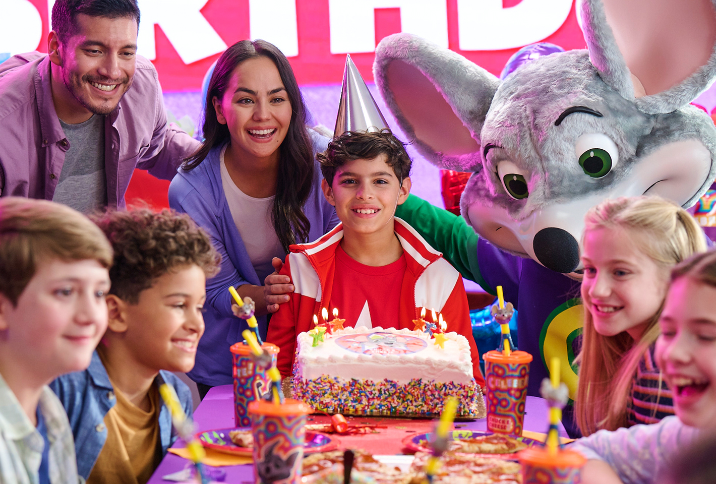 Un niño que festeja su cumpleaños rodeado por su familia, amigos, un pastel y Chuck E.