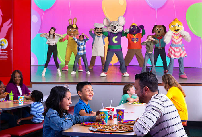 chuck e cheese y su banda realizan una presentación en la pared de video gigante mientras las familias comen pizza y disfrutan el momento