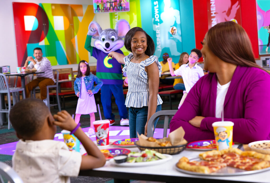 una familia comiendo pizza, mientras una niña señala la pista de baile